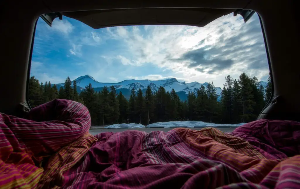 pink, white, and orange blanket inside tent near body of water and forest under gray clouds at daytime