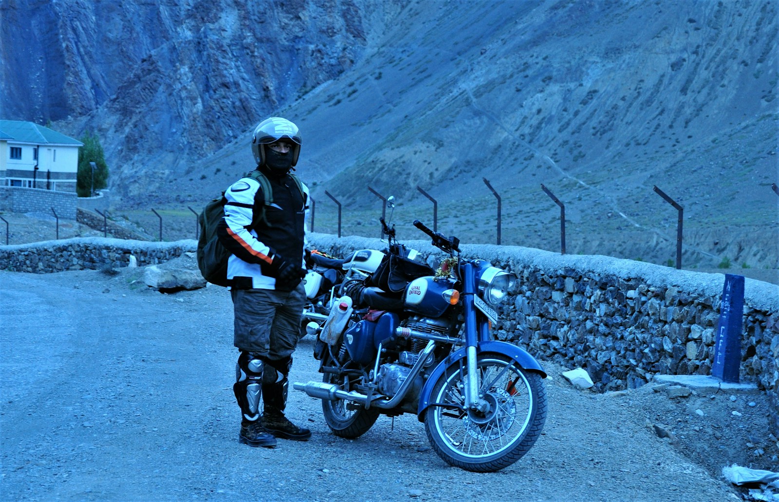 man in black jacket and black pants standing beside blue motorcycle during daytime