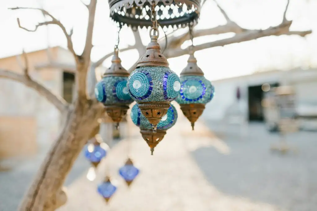 Decorative oriental lanterns of blue glass hanging on leafless tree in backyard on autumn day