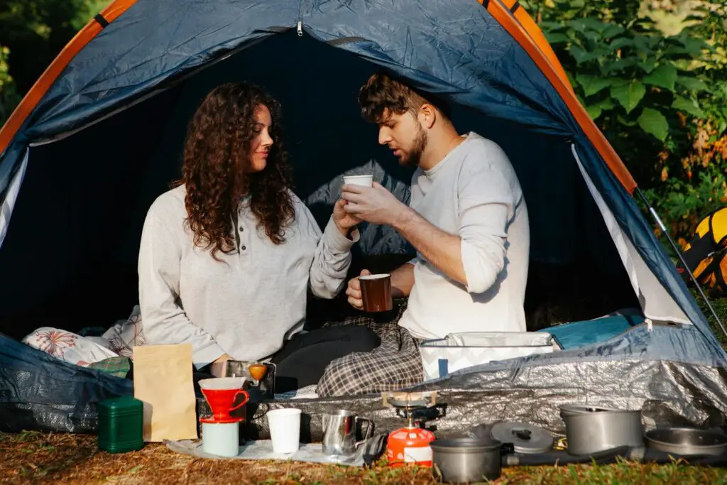 Young male hiker with hot drink interacting with female beloved while spending time in campsite