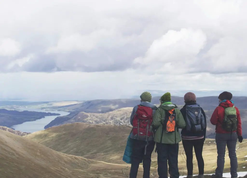 four person standing while looking on mountain view with body of water at daytime