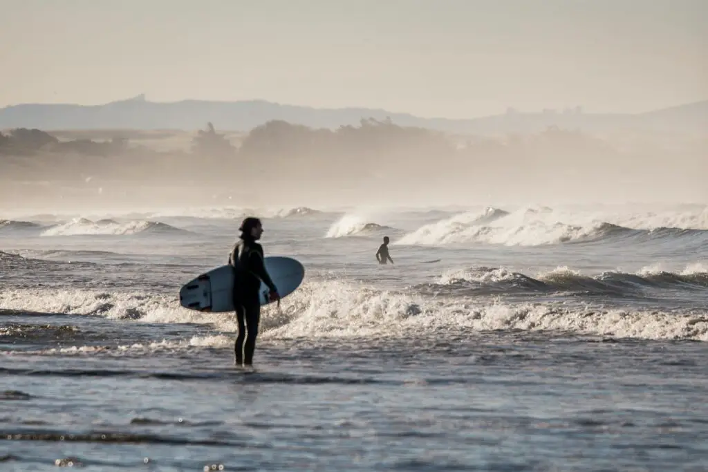 person holding white surfboard standing on body of water under gray sky during daytime